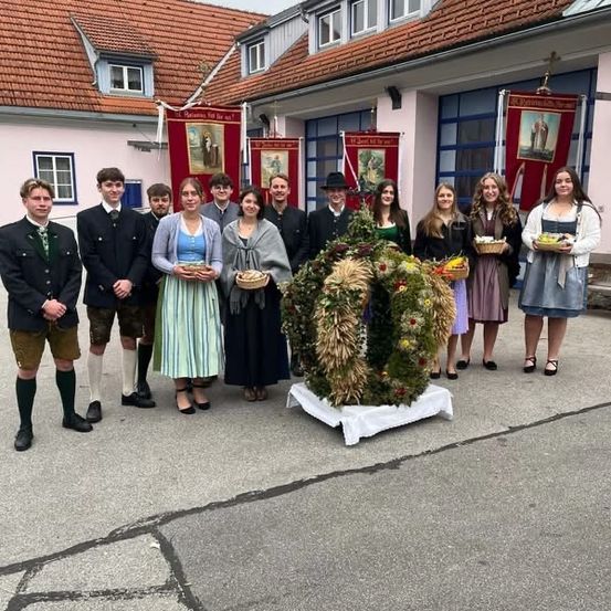 Eine Gruppe von Menschen in traditioneller Kleidung posiert für ein Foto vor einem Gebäude mit einem Kranz auf einem Tisch.