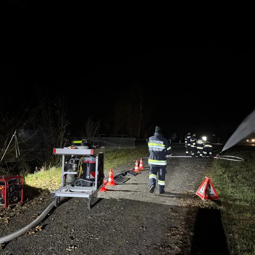 Feuerwehrleute löschen nachts ein Feuer. Ausrüstung und ein Generator sind aufgestellt. Die Szene ist von orangefarbenen Verkehrskegel umgeben.