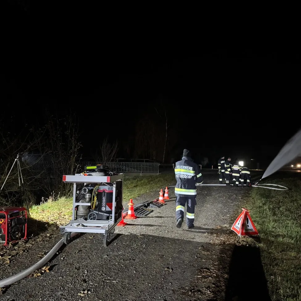 Feuerwehrleute löschen nachts ein Feuer. Ausrüstung und ein Generator sind aufgestellt. Die Szene ist von orangefarbenen Verkehrskegel umgeben.