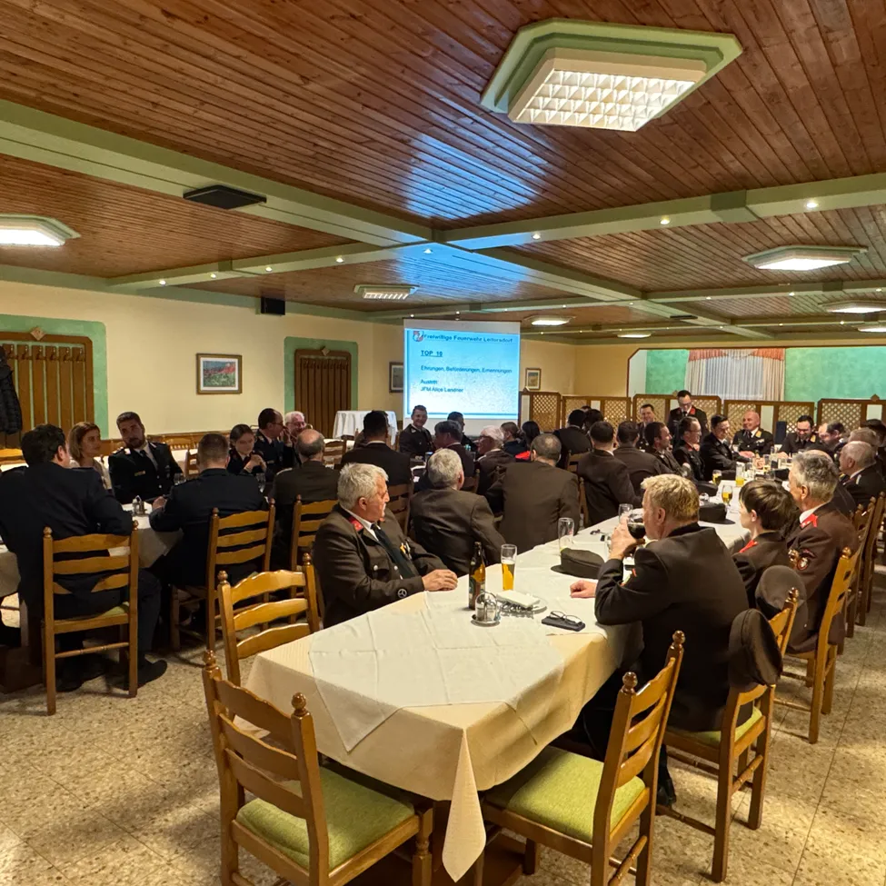 Eine Gruppe von Militäroffizieren sitzt um einen langen Tisch in einem Konferenzraum, wobei eine Projektionsleinwand Informationen dahinter anzeigt.