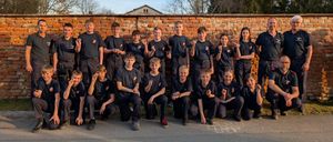 Eine Gruppe von Personen in einheitlichen Kleidungsstücken posiert für ein Foto vor einer Ziegelmauer. Sie scheinen sich in einer Schulumgebung zu befinden.