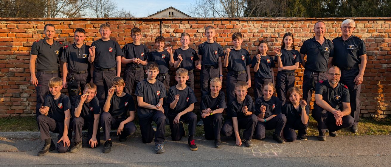 Eine Gruppe von Personen in einheitlichen Kleidungsstücken posiert für ein Foto vor einer Ziegelmauer. Sie scheinen sich in einer Schulumgebung zu befinden.