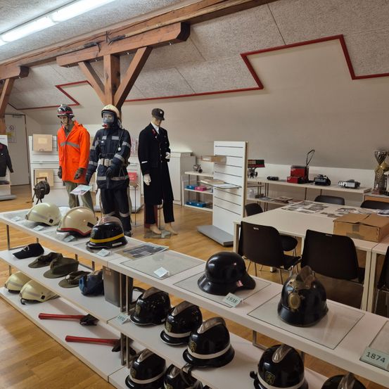 Eine Ausstellung von Helmen, Uniformen und Schutzausrüstung. Mannequins in Feuerwehr- und Polizeiuniformen ausgestellt. Eine Sammlung von Vintage-Helmen auf Regalen mit Etiketten, die Jahre angeben.