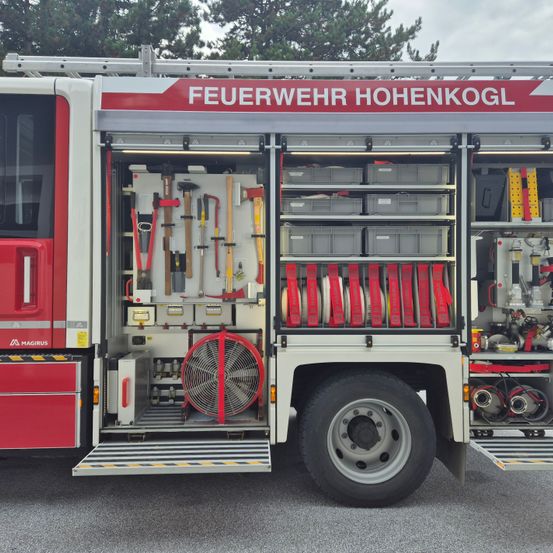 Geöffnete Ansicht eines Feuerwehrwagens mit der Aufschrift 'Feuerwehr Hohenkogl', zeigt Ausrüstungsregale, Werkzeuge und einen roten Ventilator im Inneren.