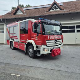 Ein roter Mercedes-Benz Feuerwehrwagen steht vor einem Gebäude mit Solarpanelen auf dem Dach. Der Wagen hat die Aufschrift 'FEUERWEHR' auf der Front.