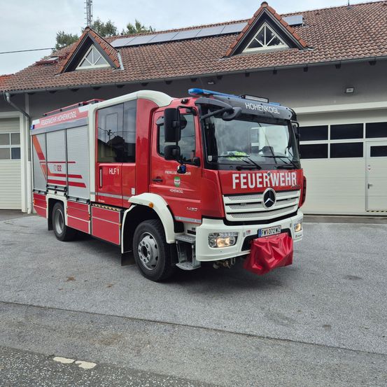 Ein roter Mercedes-Benz Feuerwehrwagen steht vor einem Gebäude mit Solarpanelen auf dem Dach. Der Wagen hat die Aufschrift 'FEUERWEHR' auf der Front.