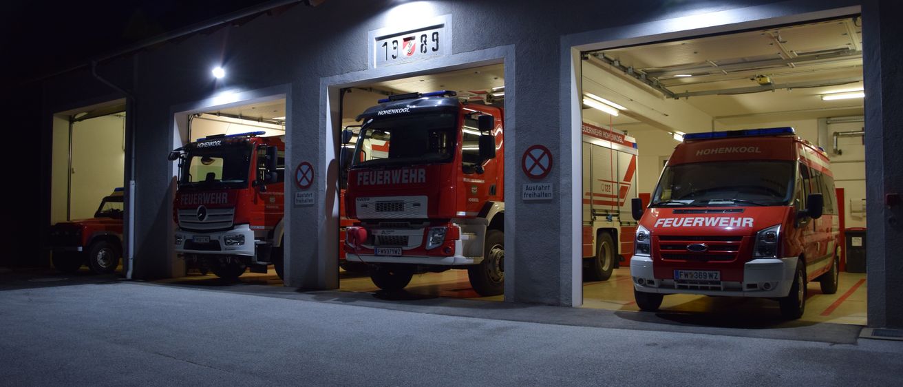 In der Nacht ist eine Feuerwache mit drei Notfallfahrzeugen im Inneren geparkt. Das mittlere Fahrzeug hat die Nummer 13.7.89. Es gibt Schilder, die Rauchen und Fahren verbieten.