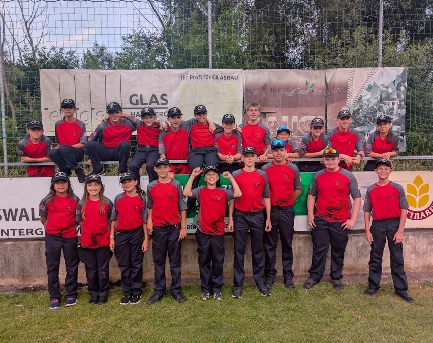 Eine Gruppe junger Athleten in roten und grauen Uniformen posiert für ein Foto vor einem Banner im Hintergrund.