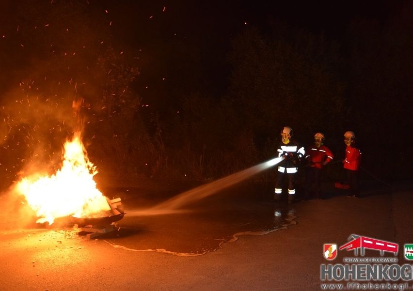 Feuerwehrleute in Schutzkleidung löschen bei Nacht einen Brand mit einer Wasserleitung.