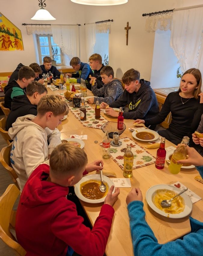 Eine Gruppe junger Jungen sitzt um einen Tisch in einem Raum und isst. Einige von ihnen tragen Kapuzenpullover.