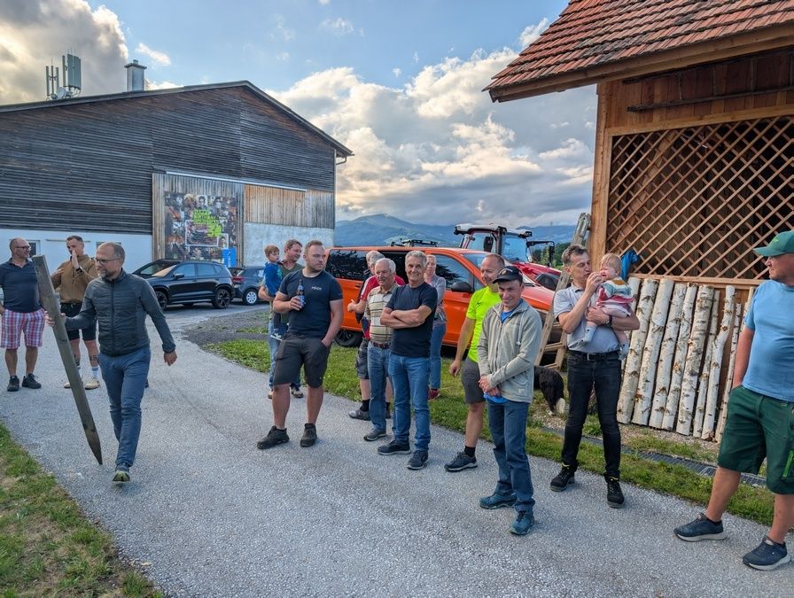 Eine Gruppe von Menschen steht vor einem Gebäude mit einem Bild an der Wand, geparkten Autos davor und Bergen in der Ferne.