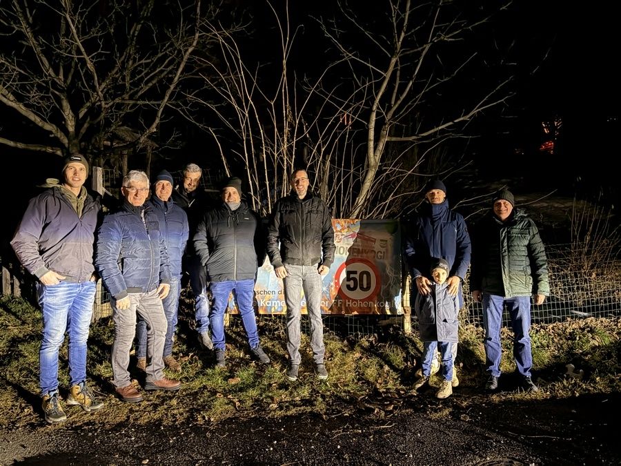 Eine Gruppe von Männern und einem Kind steht nachts vor einem Schild mit 50 km/h Geschwindigkeitsbegrenzung.
