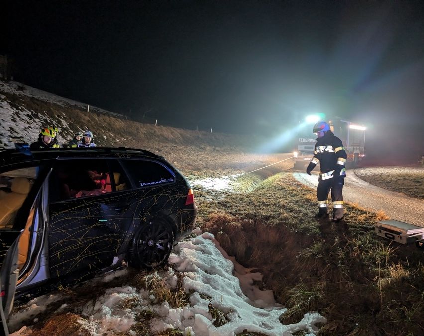 Notfallhelfer sind nachts an einer verschneiten Straße unterwegs und helfen einem Auto, das in eine Grube gefallen ist.