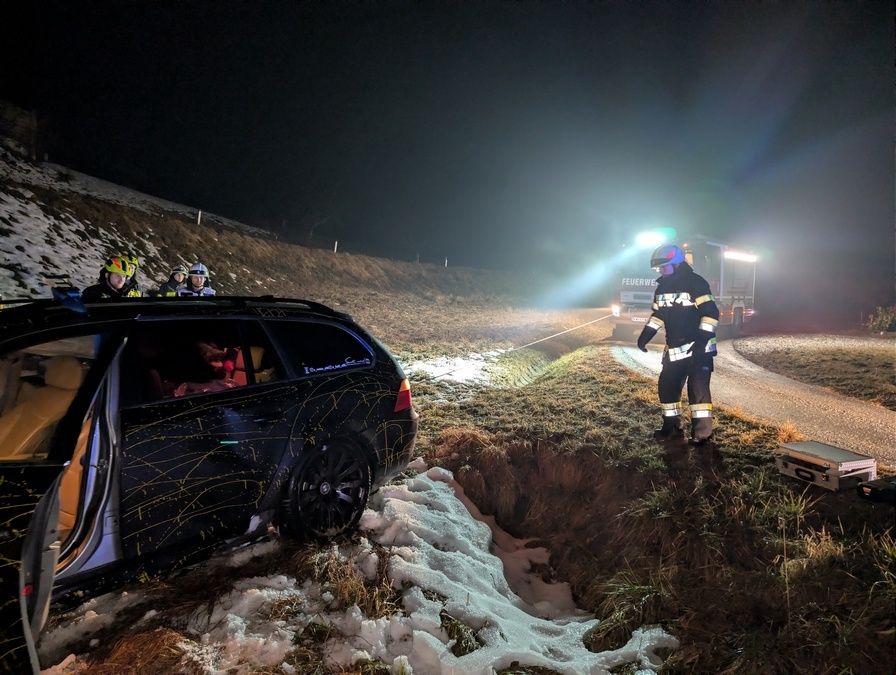 Notfallhelfer sind nachts an einer verschneiten Straße unterwegs und helfen einem Auto, das in eine Grube gefallen ist.