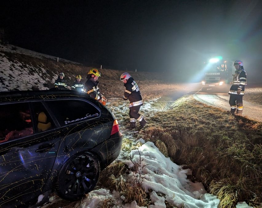Feuerwehrleute helfen einer Person in einem verunglückten Auto, umgeben von Schnee, mit einem Feuerwehrfahrzeug in der Nähe.