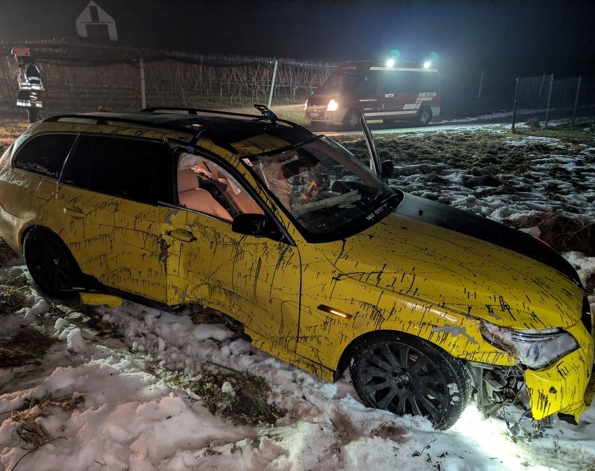 Ein gelbes Auto ist im Schnee verunglückt, ein Rettungsfahrzeug im Hintergrund.