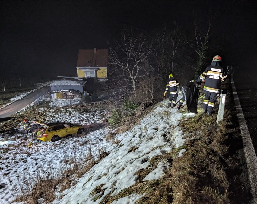 Rettungskräfte in Schutzausrüstung arbeiten am Unfallort eines Autounfalls auf einer verschneiten Straße. Ein gelbes Auto ist an der Straßenseite beschädigt.