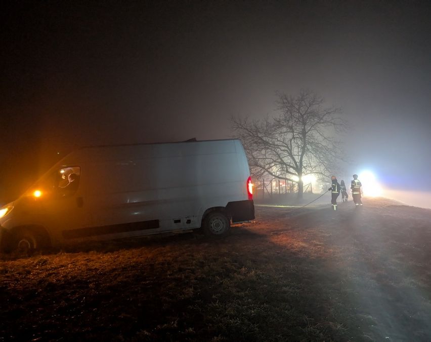 In der nebligen Nacht steht ein weißer Lieferwagen am Straßenrand. Drei Feuerwehrleute ziehen eine Schlange. Sie sind in voller Ausrüstung. Das Gebiet ist dunkel, und das einzige Licht kommt vom Lieferwagen und den Feuerwehrleuten.