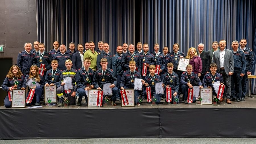 Eine Gruppe von Menschen in Uniformen posiert für ein Foto auf der Bühne und hält Urkunden und Medaillen in den Händen.