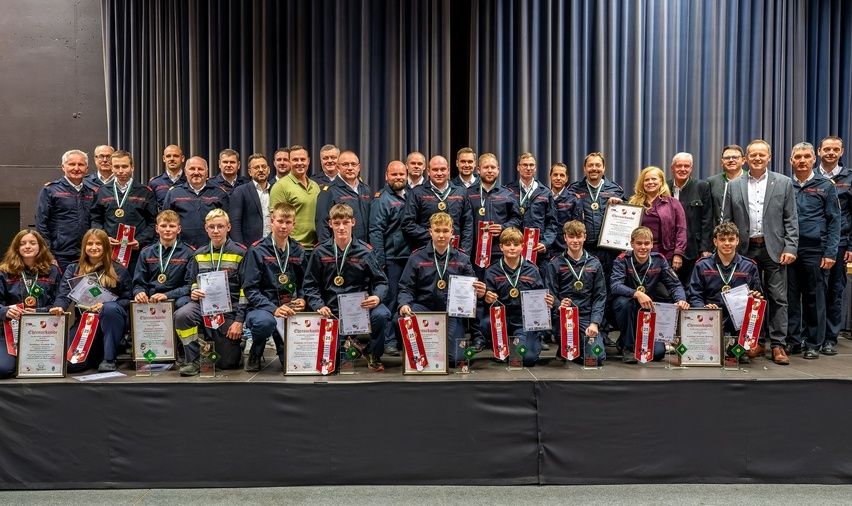 Eine Gruppe von Menschen in Uniformen posiert für ein Foto auf der Bühne und hält Urkunden und Medaillen in den Händen.