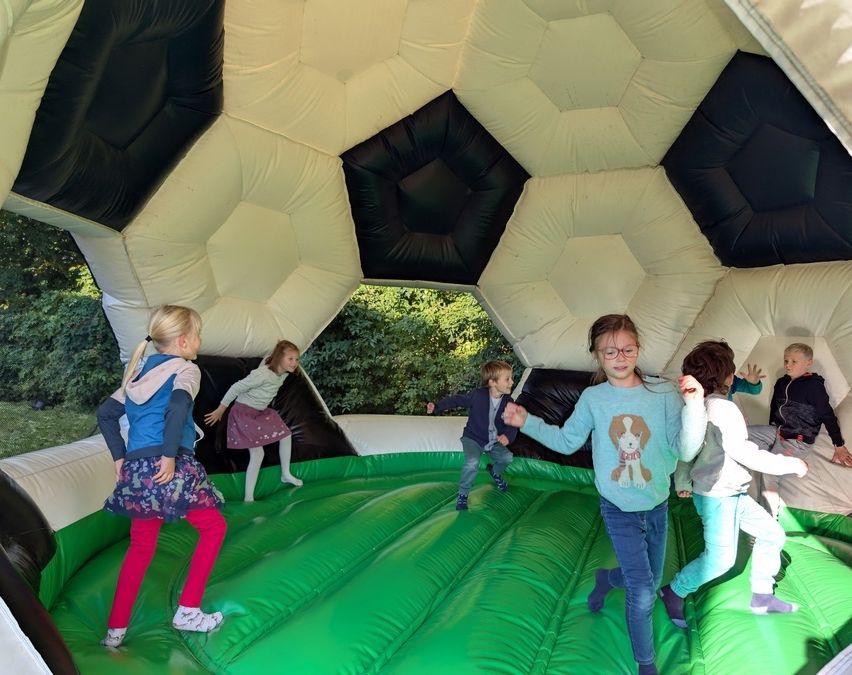 Fünf Kinder spielen in einem grünen, fußballförmigen Hüpfhaus. Sie springen und haben Spaß.