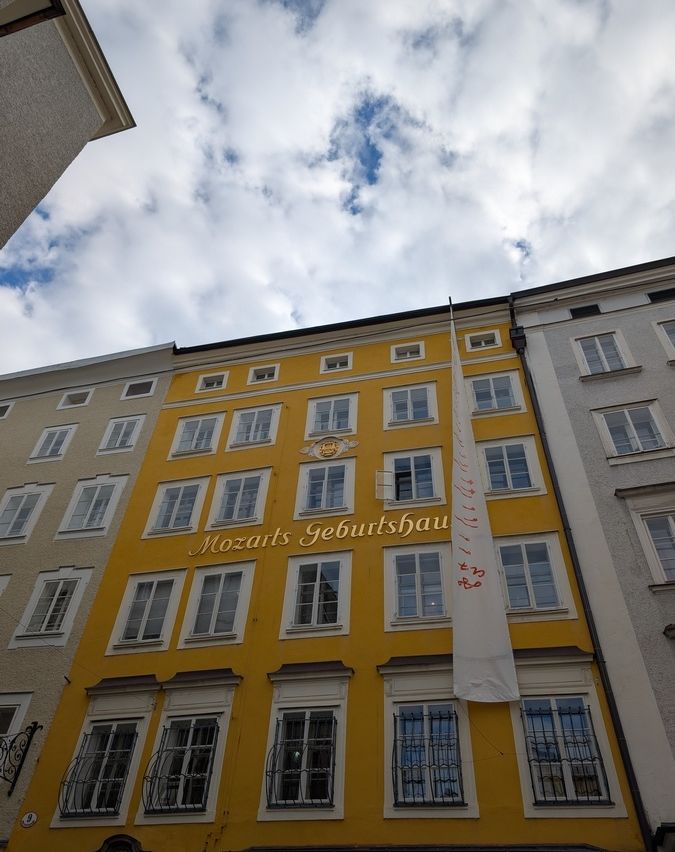 Ein gelbes Gebäude mit mehreren Fenstern. Es steht 'Mozarts Geburtshaus'. An der Seite befindet sich eine Fahne.