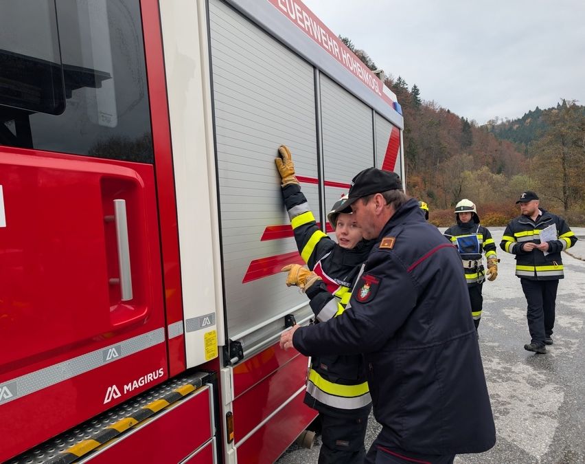 Ein Feuerwehrmann zeigt einem Kind, wie man die Tür eines Feuerwehrwagens mit dem Wort Magirus an der Seite öffnet.
