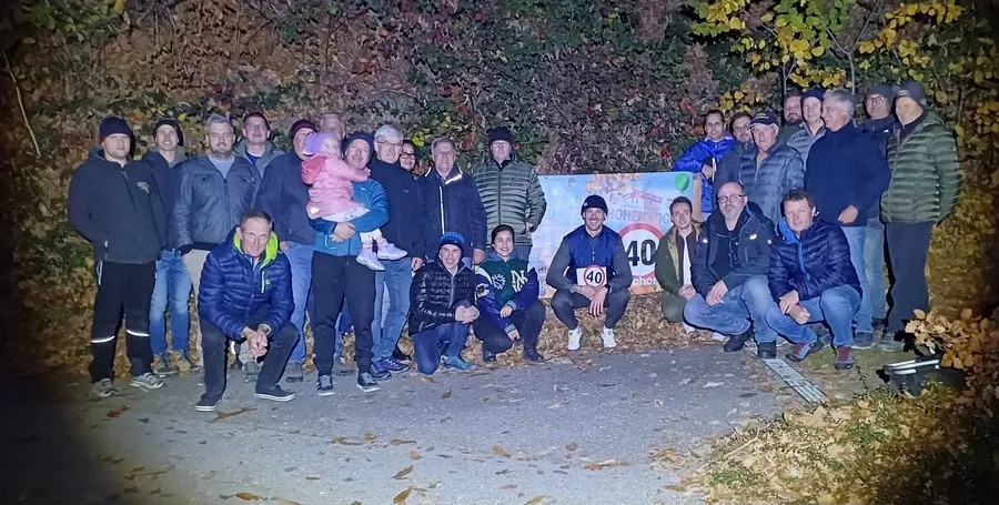 Eine Gruppe von Menschen, darunter Männer, Frauen und ein Kind, posiert für ein Foto auf einer Straße mit einem Schild, das eine Geschwindigkeitsbegrenzung von 40 km/h anzeigt.