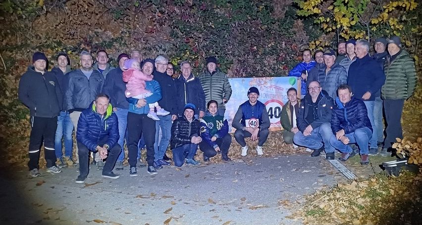 Eine Gruppe von Menschen, darunter Männer, Frauen und ein Kind, posiert für ein Foto auf einer Straße mit einem Schild, das eine Geschwindigkeitsbegrenzung von 40 km/h anzeigt.