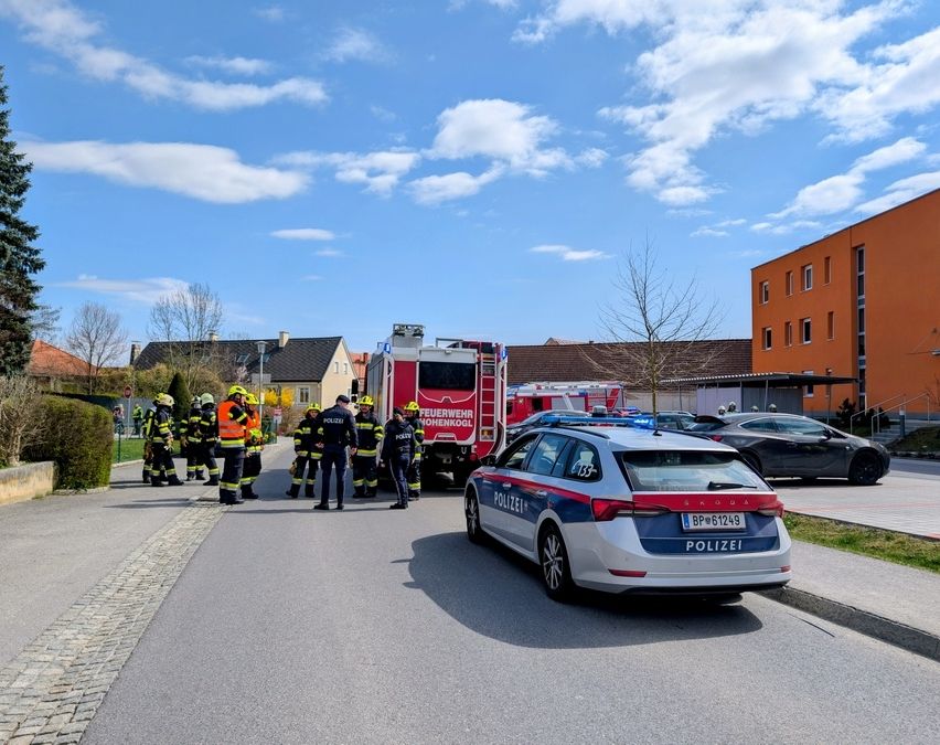 Ein Feuerwehrauto und ein Polizeiauto sind am Straßenrand geparkt, Feuerwehrleute und Polizeibeamte stehen herum.