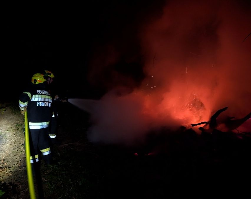 Zwei Feuerwehrleute in Schutzkleidung bekämpfen nachts ein Feuer und verwenden Schläuche, um die Flammen zu löschen.