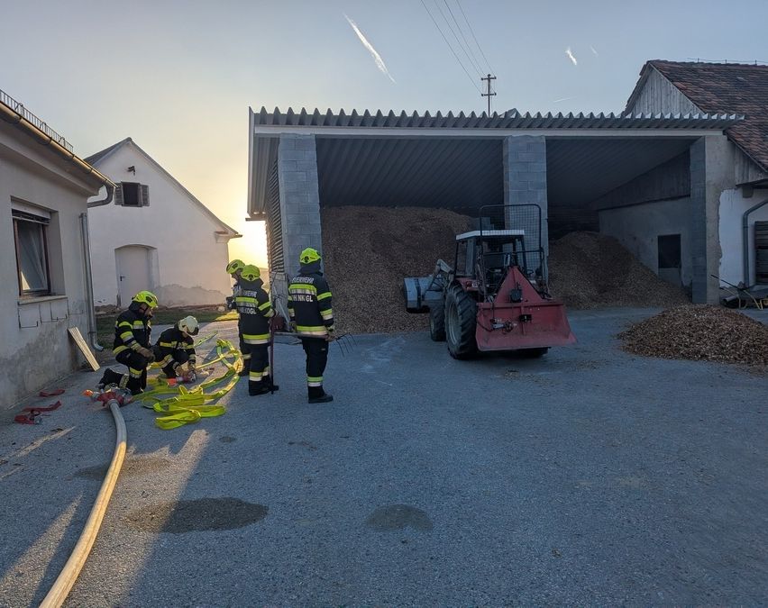 Feuerwehrleute bereiten sich mit Schläuchen und einem Traktor vor, ein Feuer vor einer Scheune zu löschen.