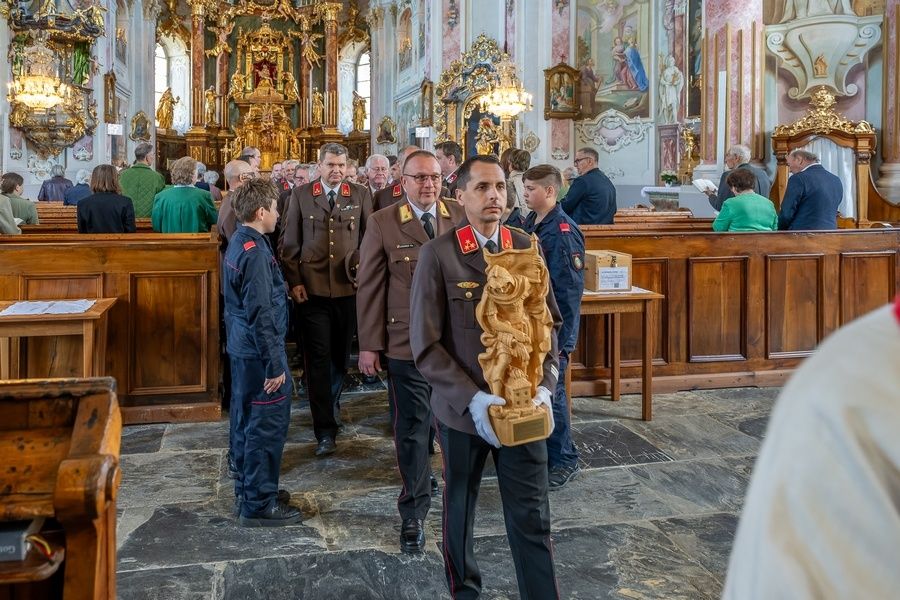 Eine Gruppe von Männern in Uniformen, die in einer Kirche mit einem hölzernen Altar und Dekorationen im Hintergrund gehen.