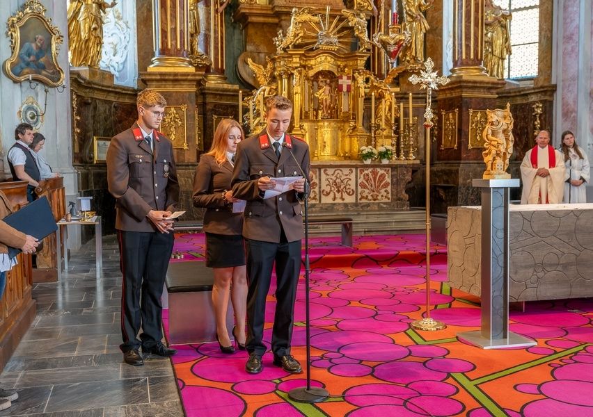 Eine feierliche Zeremonie in einer Kirche, bei der zwei Personen aus einem Papier lesen. Ein Priester steht vor dem Altar.
