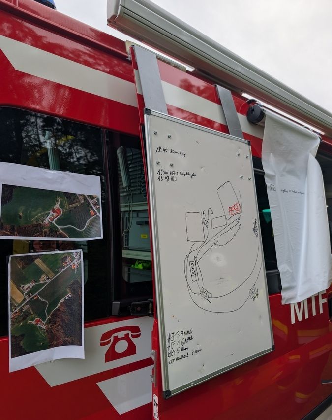 A red vehicle has a whiteboard with a diagram and text. Two pictures are attached to the side. A red telephone is on the door. A white cloth hangs from the top.