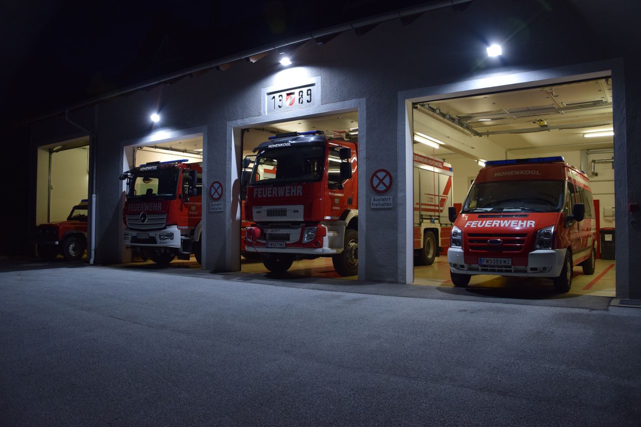 Drei Feuerwehrfahrzeuge stehen in einer Garage. Das mittlere hat die Nummer 89 auf der Front, während die anderen die Nummern 13 und 78 tragen.