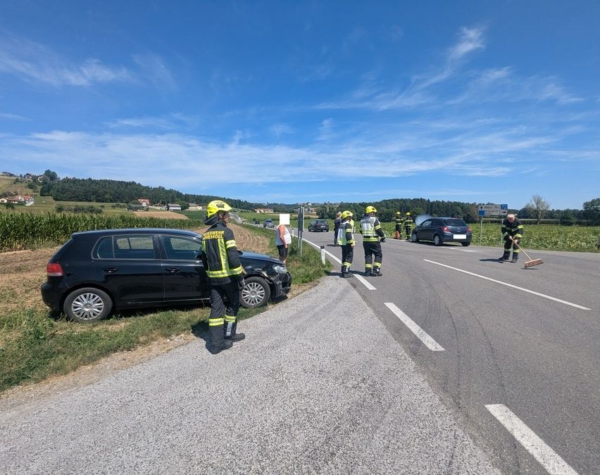 Eine Gruppe von Feuerwehrleuten in gelben Helmen reinigt die Straße nach einem Autounfall. Das Auto ist am Straßenrand geparkt.