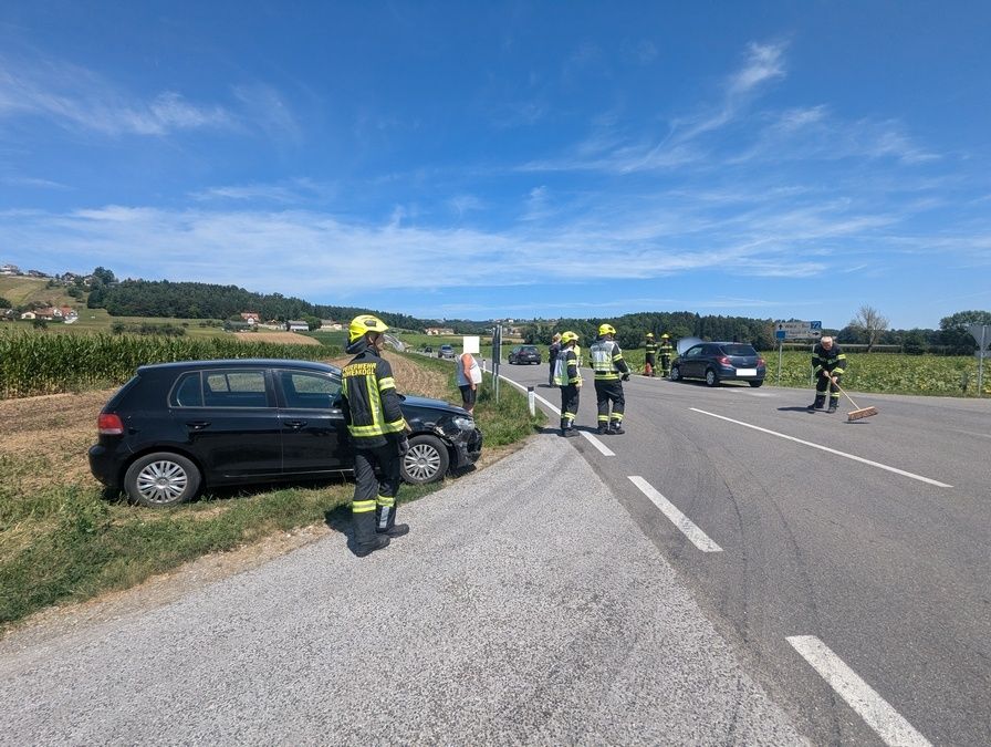 Eine Gruppe von Feuerwehrleuten in gelben Helmen reinigt die Straße nach einem Autounfall. Das Auto ist am Straßenrand geparkt.