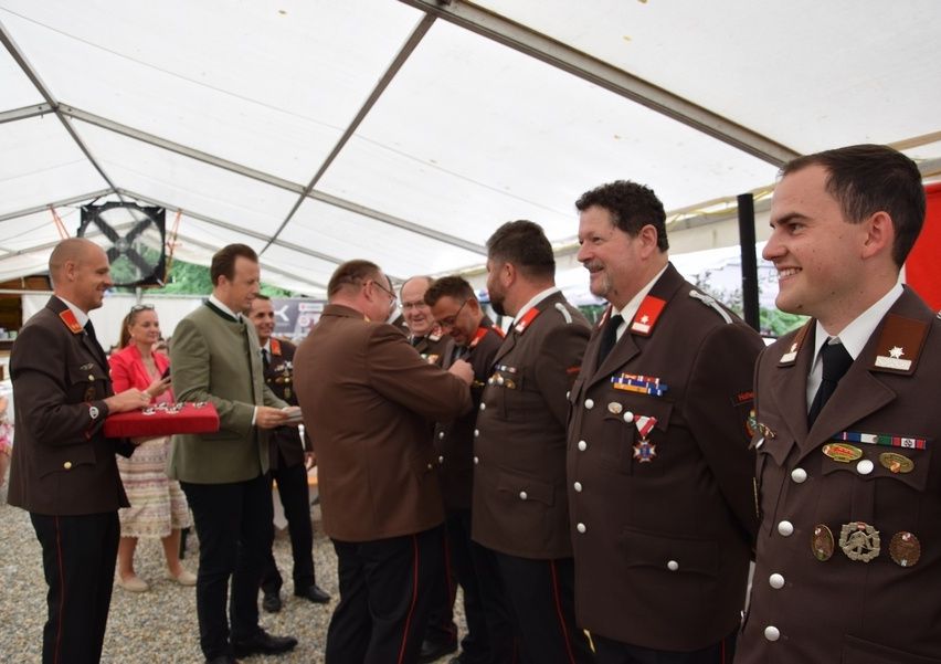 Eine Gruppe von Männern in Militäruniformen steht unter einem Zelt, möglicherweise während einer Preisverleihung. Ein Mann hält eine rote Box und ein anderer erhält eine Auszeichnung.