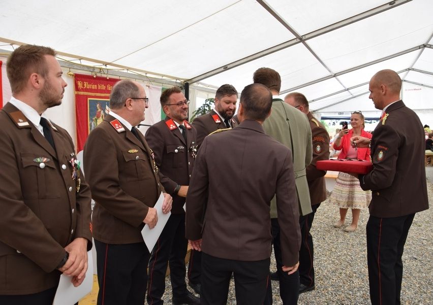Eine Gruppe uniformierter Männer und eine Frau stehen in einem Zelt, möglicherweise bei einer militärischen Veranstaltung. Sie führen ein Gespräch.