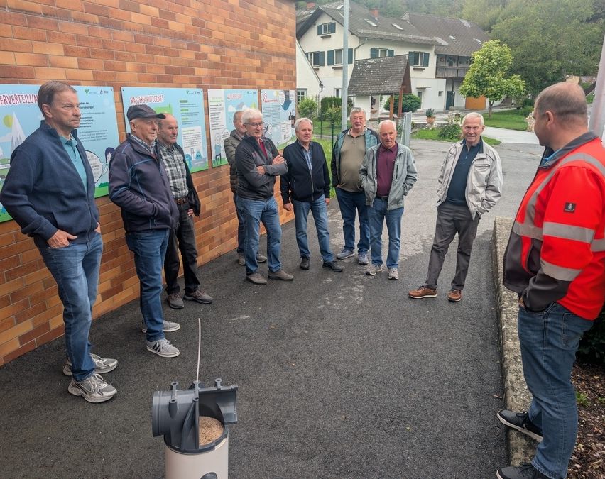 Eine Gruppe älterer Männer steht vor einer Ziegelwand mit Plakaten und diskutiert mit einem Mann in einer Warnweste.