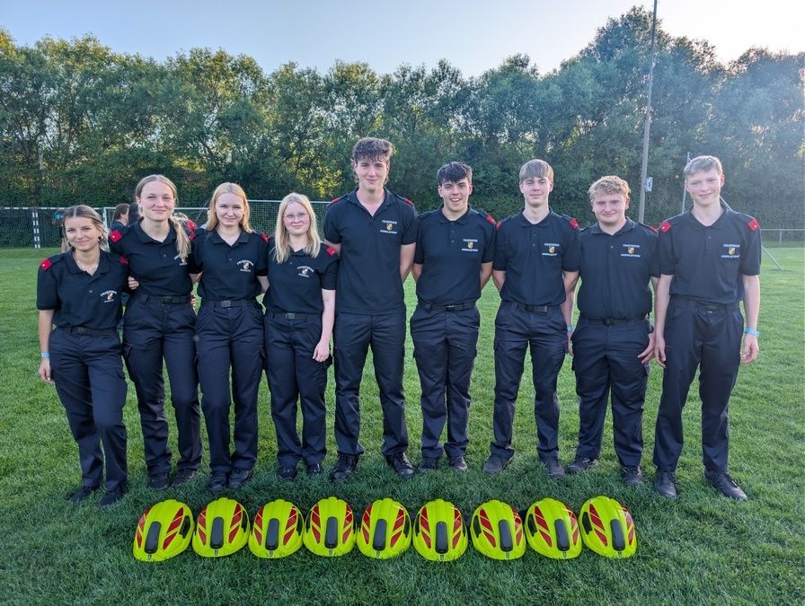 Eine Gruppe junger Menschen in Uniform posiert für ein Foto auf einem grünen Feld mit gelben Helmen davor.