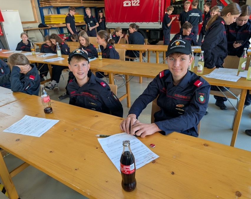 Zwei junge Leute in Uniform sitzen an einem Tisch mit Papieren und einer Flasche Coca-Cola.