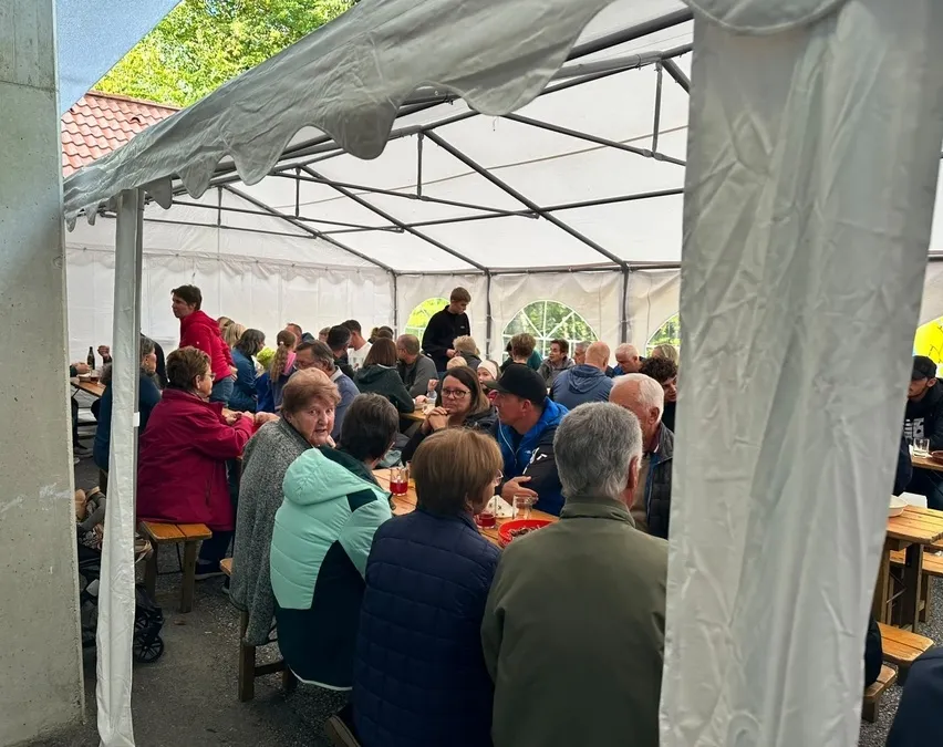 Eine Gruppe von Menschen sitzt um Tische in einem Zelt, einige unterhalten sich und andere essen.