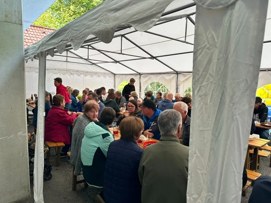 Eine Gruppe von Menschen sitzt um Tische in einem Zelt, einige unterhalten sich und andere essen.