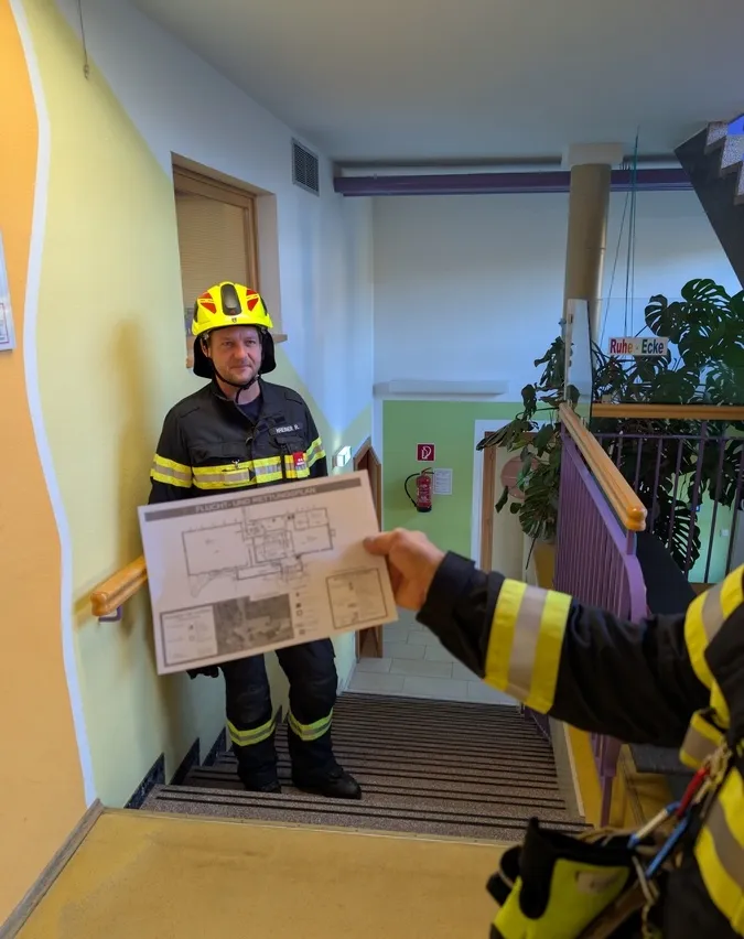 Ein Feuerwehrmann steht auf der Treppe und hält eine Papierkarte des Gebäudes.