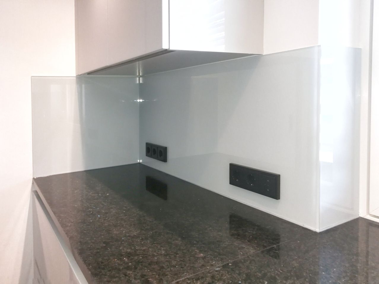 Eine moderne Küche mit weißen Schränken, einer schwarzen Granitarbeitsplatte und weißen Wänden. Zwei Steckdosen sind an der Wand montiert.