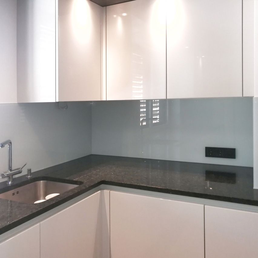 Eine moderne Küche mit weißen Schränken, einer Granitarbeitsplatte, einem Edelstahlspülbecken und einem schlanken Wasserhahn. Die Wand hat ein milchiges Glasdesign.
