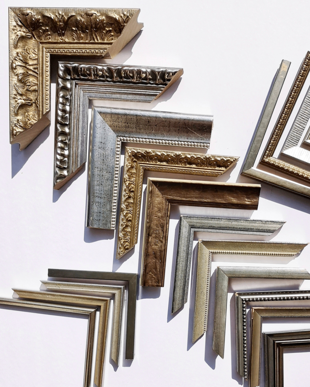 Eine Sammlung verzierter Bilderrahmen in Gold und Silber mit komplizierten Designs, auf einer weißen Oberfläche angeordnet.