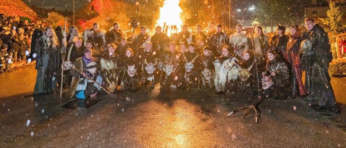 Eine Gruppe von Menschen in Kostümen posiert für ein Foto vor einem großen Scheiterhaufen an einem verschneiten Abend.